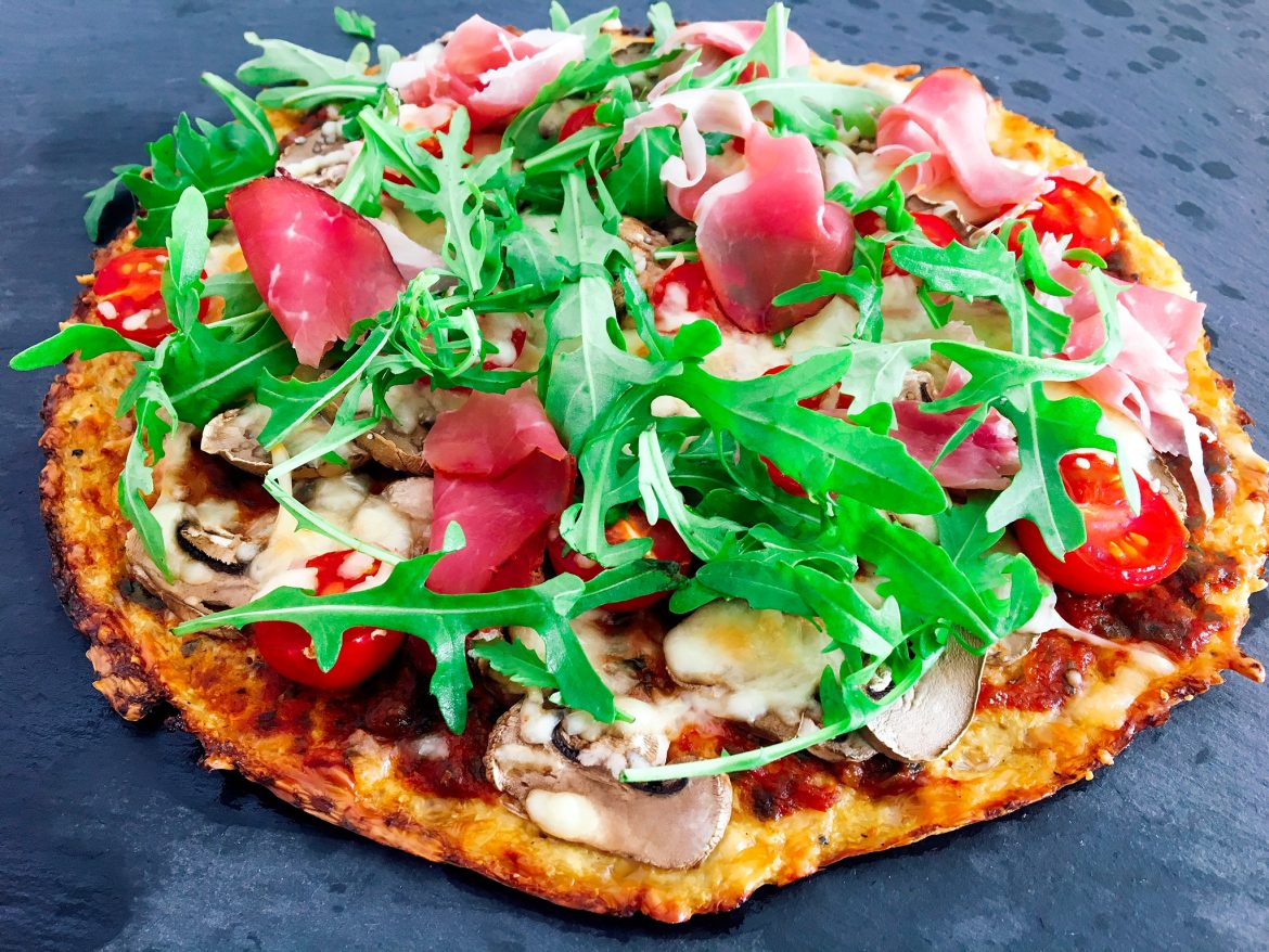 Lowcarb Pizza aus Blumenkohlsraspeln, belegt mit Champignons, Rucola und Serranoschinken