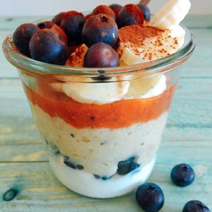 Geschichtetes Erdbeer-Rahabarber-Porridge im Glas mit Skyr und frischen blaubeeren und Bananen